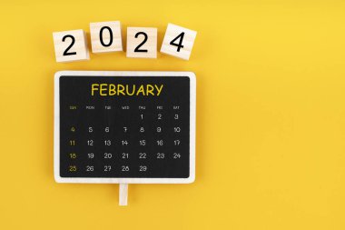 Şubat 2024 için sarı arkaplan üzerinde kopya alanı olan siyah karatahta takvimi.