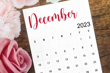 2023 Aralık ayının takvimi. Ahşap arka planda pembe gül var..