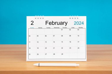 2024 yılı için Şubat ayının masa takvimi ve mavi arkaplan ile ahşap masa üzerinde kalem.