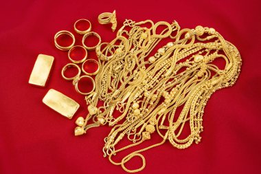 Kırmızı kadife arka planda bir sürü altın kolye ve altın külçeler..
