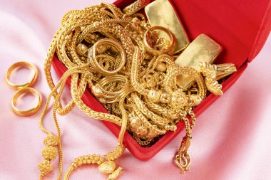 Birçok altın kolye ve altın külçeler kırmızı kutuda kadife kumaş arka planda.