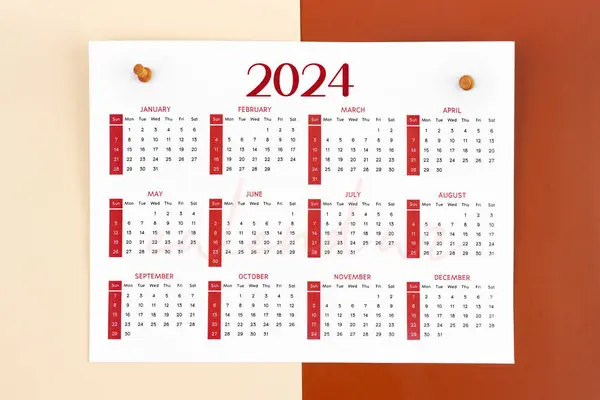12 months calendar page for 2024 year and wooden pins on red background.
