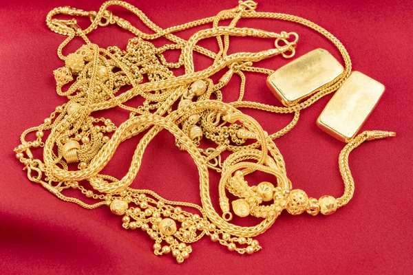 Many gold necklaces and gold bars on red velvet cloth background.