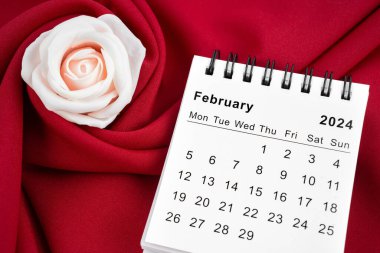 Şubat 2024 masa takvimi ve kırmızı tekstil arka planında pembe gül.