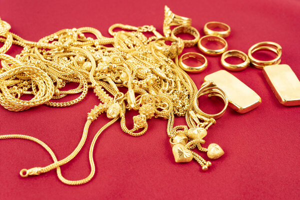 Many gold necklaces and gold bars on red velvet cloth background.