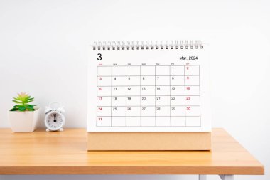 2024 yılı için Mart ayının masa takvimi ve ahşap masa üzerindeki çalar saat..