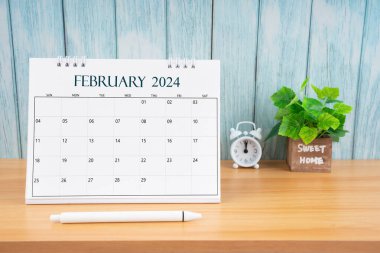 2024 yılının Şubat ayı masa takvimi ve ahşap masa üzerindeki çalar saat..