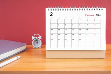 2024 yılının Şubat ayı masa takvimi ve ahşap masa üzerindeki çalar saat..