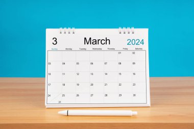 2024 yılı için aylık masa takvimi Mart ve mavi arkaplan ile ahşap masa üzerinde kalem.
