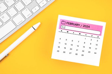 2024 yılının Şubat 2024 takvimi ve sarı arkaplanda kalemli bilgisayar klavyesi.