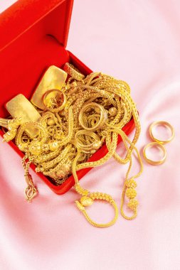 Pembe kadife arka planda kırmızı kutuda bir sürü altın kolye ve altın külçeler var..