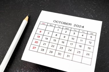 Ekim 2024 için beyaz takvim sayfası ve siyah arkaplan üzerine kalem.