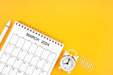 Mart 2024, 2024 için aylık masa takvimi ve sarı arka planda ataçları olan alarm saati. Kopyalama alanı olan konum.