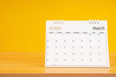 Mart 2024, 2024 tarihli aylık masa takvimi sarı arka planlı ahşap masa üzerinde..