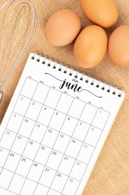 Haziran 2024 Masa takvimi ve arka planda yumurta çırpma kabuğu olan taze yumurtalar.