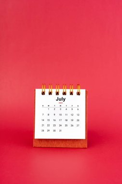 Kırmızı arkaplanda Temmuz 2024 beyaz masa takvimi.