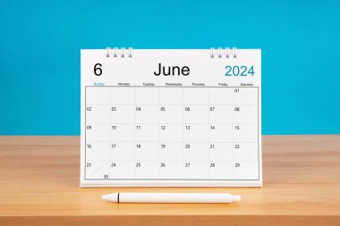 2024 yılı için Haziran aylık masa takvimi ve mavi arkaplan ile ahşap masa üzerinde kalem.