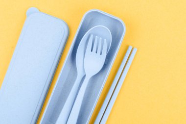 Sarı arka planda plastik kaşıklar, çatallar ve çubuklar..