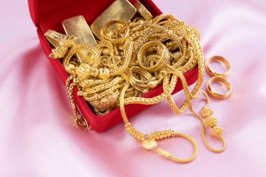 Pembe kumaş arka planda kırmızı kadife kutuda altın kolye ve yüzükler..