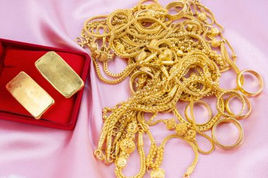 Pembe kadife arka planda kırmızı kutuda bir sürü altın kolye ve altın külçeler var..