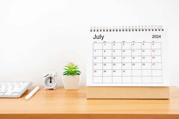 stock image July 2024, Monthly desk calendar for 2024 year on wooden table with alarm clock.