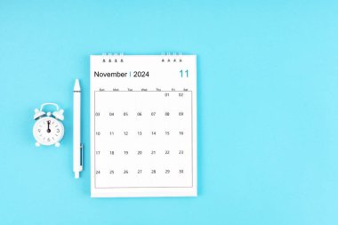 Kasım 2024, 2024 yılı için aylık masa takvimi ve mavi arkaplan üzerinde alarm saati olan kalem.