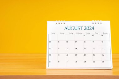 Ağustos 2024, 2024 tarihli aylık masa takvimi sarı arka planlı ahşap masada..