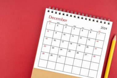 Aralık 2024 kırmızı arkaplan üzerinde masa takvimi ve kalem.