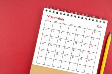 Kasım 2024 kırmızı arkaplan üzerinde masa takvimi ve kalem.