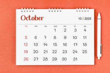 Ekim 2025 2025 Aylık masa takvimi ve kırmızı arkaplan üzerine kalem.