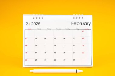 Şubat 2025, 2025 yılı için aylık masa takvimi ve sarı arkaplan üzerine kalem.