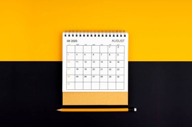 Sarı ve siyah arkaplan üzerinde Ağustos 2025 masa takvimi ve kalemin üst görünümü.