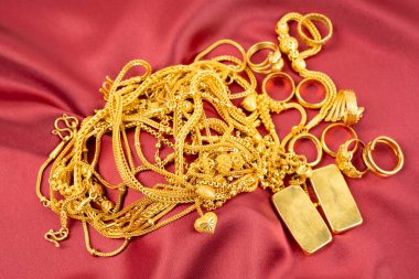 Kırmızı kadife arka planda bir sürü altın kolye ve altın külçeler..