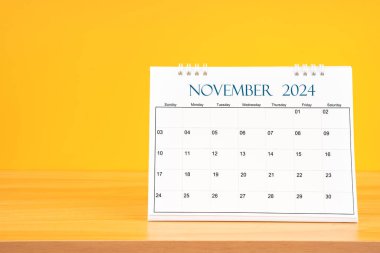 Kasım 2024, 2024 tarihli aylık masa takvimi sarı arka planlı ahşap masa üzerinde..