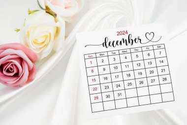 Aralık 2024 takvim sayfası ve gül çiçeği beyaz saten tekstil arkaplanı.