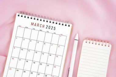 Mart 2025 takvim ve pembe kumaş arka planında açık günlüğü olan kalem. Aylık takvim kavramı.