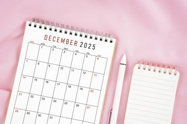 Aralık 2025 takvim ve pembe kumaş arka planında açık günlüğü olan kalem. Aylık takvim kavramı.