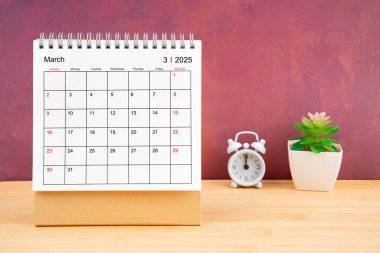 2025 yılı için March Monthly masa takvimi ve kırmızı arkaplan ile ahşap masa üzerindeki alarm saati.