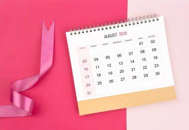 Ağustos 2025 masa takvimi ve pembe arkaplan üzerine pembe kurdele.