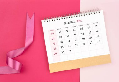 Aralık 2024 Masa takvimi ve pembe arkaplan üzerine pembe kurdele.