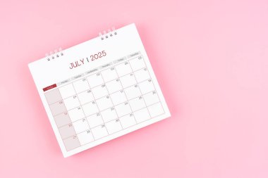 Randevu almak için 2025 yılının temmuz ayının masa başı takviminin üst görünümü pembe zemin üzerinde.