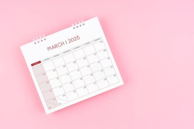 Randevu almak için 2025 Mart ayının masa başı takviminin üst görünümü pembe arka planda.