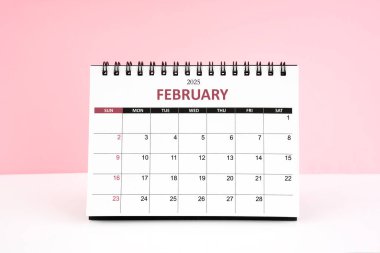 Şubat 2025 Masa takvimi pembe arkaplanlı beyaz masa üzerinde.