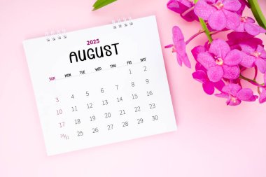 Pembe arka planda bir Ağustos 2025 masa takvimi ve pembe orkide.