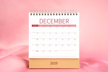 Pembe renkli tekstil üzerine boş Aralık 2025 masa takvimi ön görünümü.
