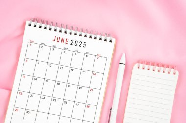 Haziran 2025 takvim ve pembe kumaş arka planında açık günlüğü olan kalem. Aylık takvim kavramı.