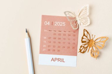 Nisan 2025 Sarı zemin üzerinde planlamak ve hatırlatmak için düzenleyici takvim kartı ve kelebek kağıt.