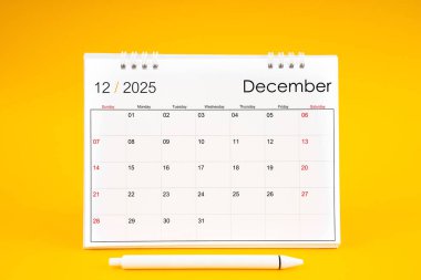Aralık 2025, 2025 yılı için aylık masa takvimi ve sarı arkaplan üzerine kalem.