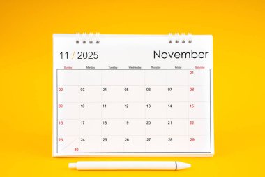 Kasım 2025, 2025 yılı için aylık masa takvimi ve sarı arkaplan üzerine kalem.