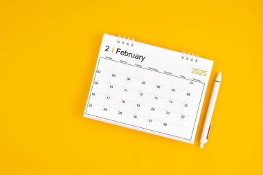 Şubat 2025, 2025 yılı için aylık masa takvimi ve sarı arkaplan üzerine kalem.